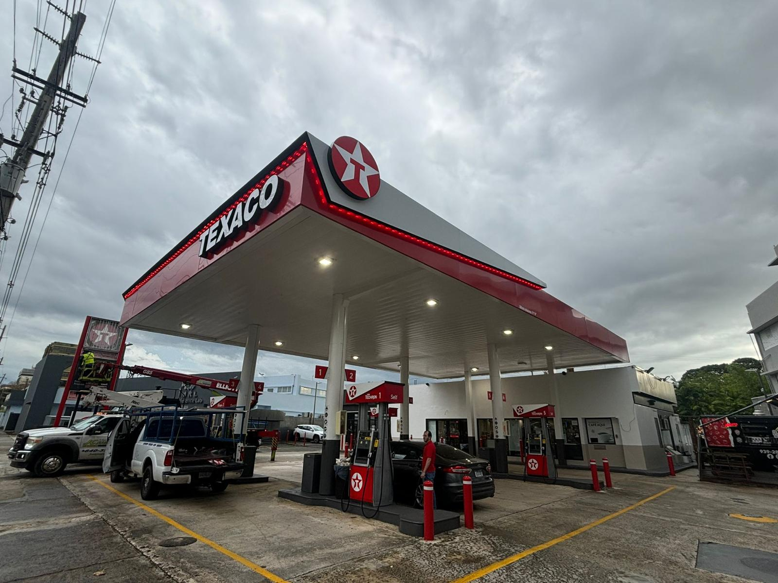 Estación de gasolina Texaco con varias bombas y vehículos, bajo un cielo nublado.