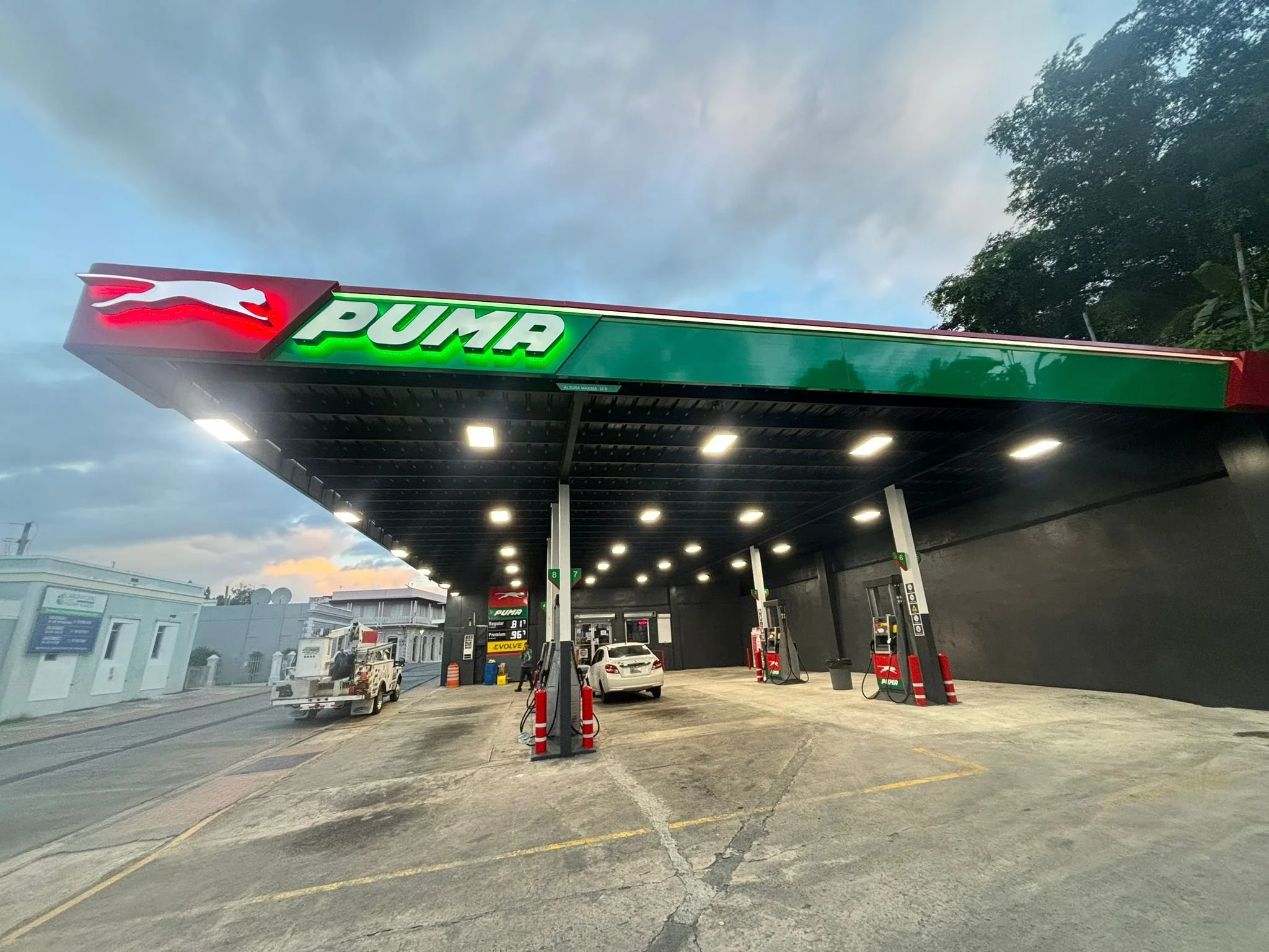 Estación de gasolina de la marca PUMA con varias bombas y autos cargando combustible, en una tarde con cielo parcialmente nublado.