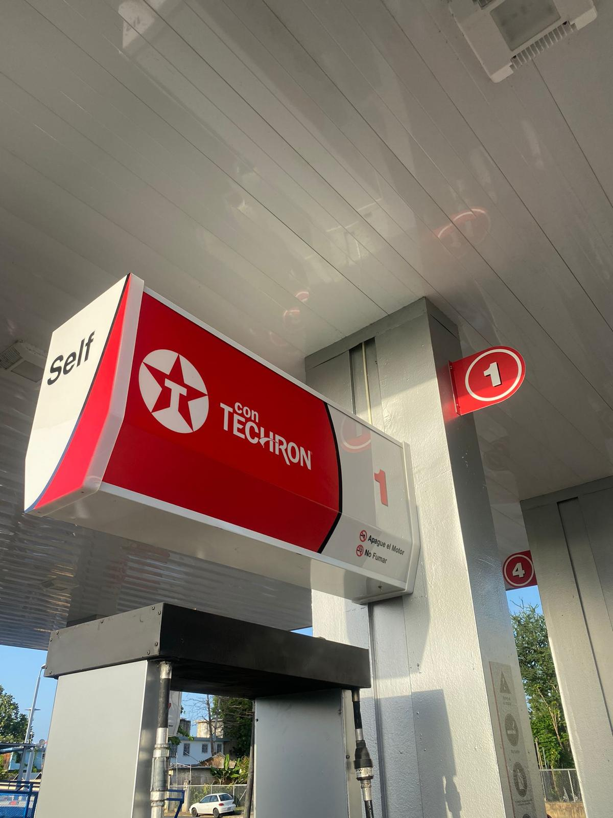 Estación de gasolina con señal redonda que tiene el número 1, indicando la bomba de combustible, y cartel que dice 'Self con TECRON'.