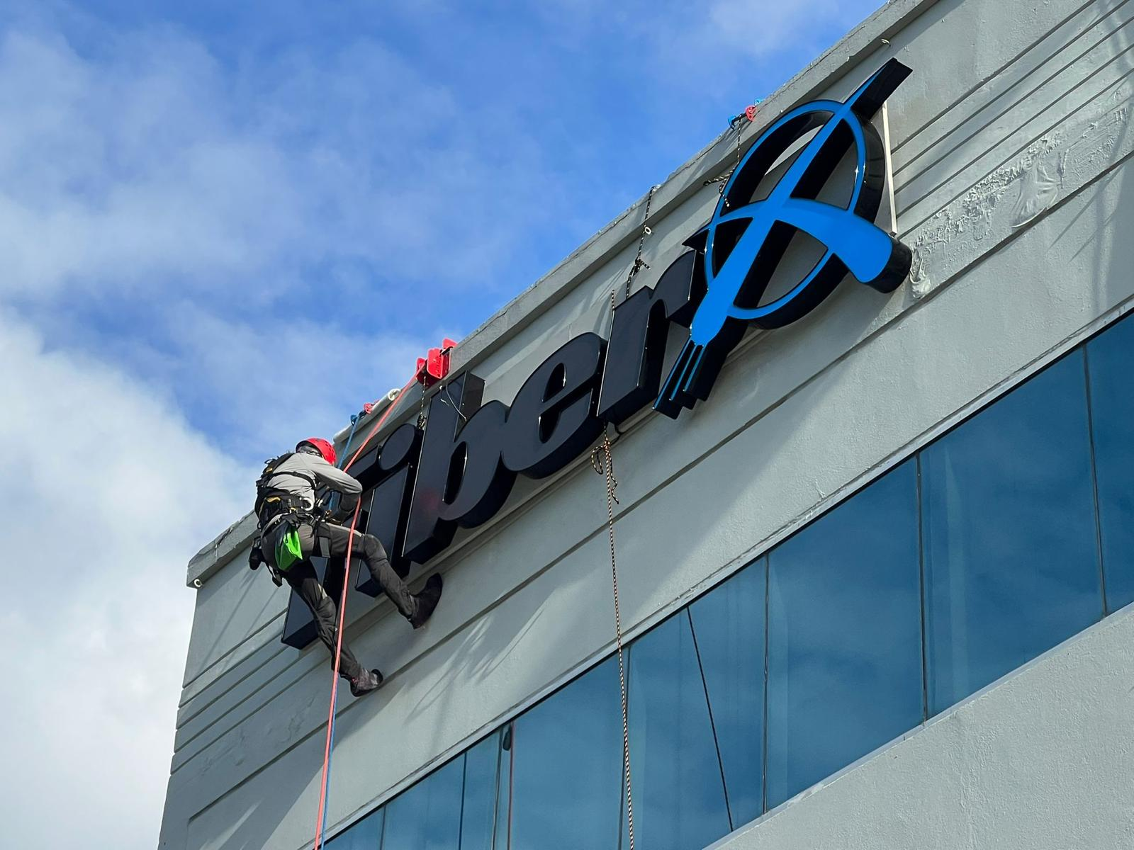 Un trabajador instala o remueve un letrero en el exterior de un edificio moderno.