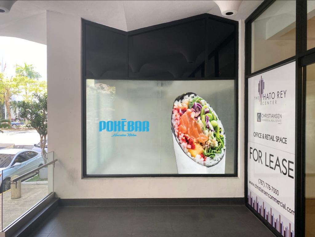 Publicidad en una ventana con un logo de Pokébar y una imagen de un bol de comida, posiblemente sushi o poke, en un espacio comercial en alquiler.