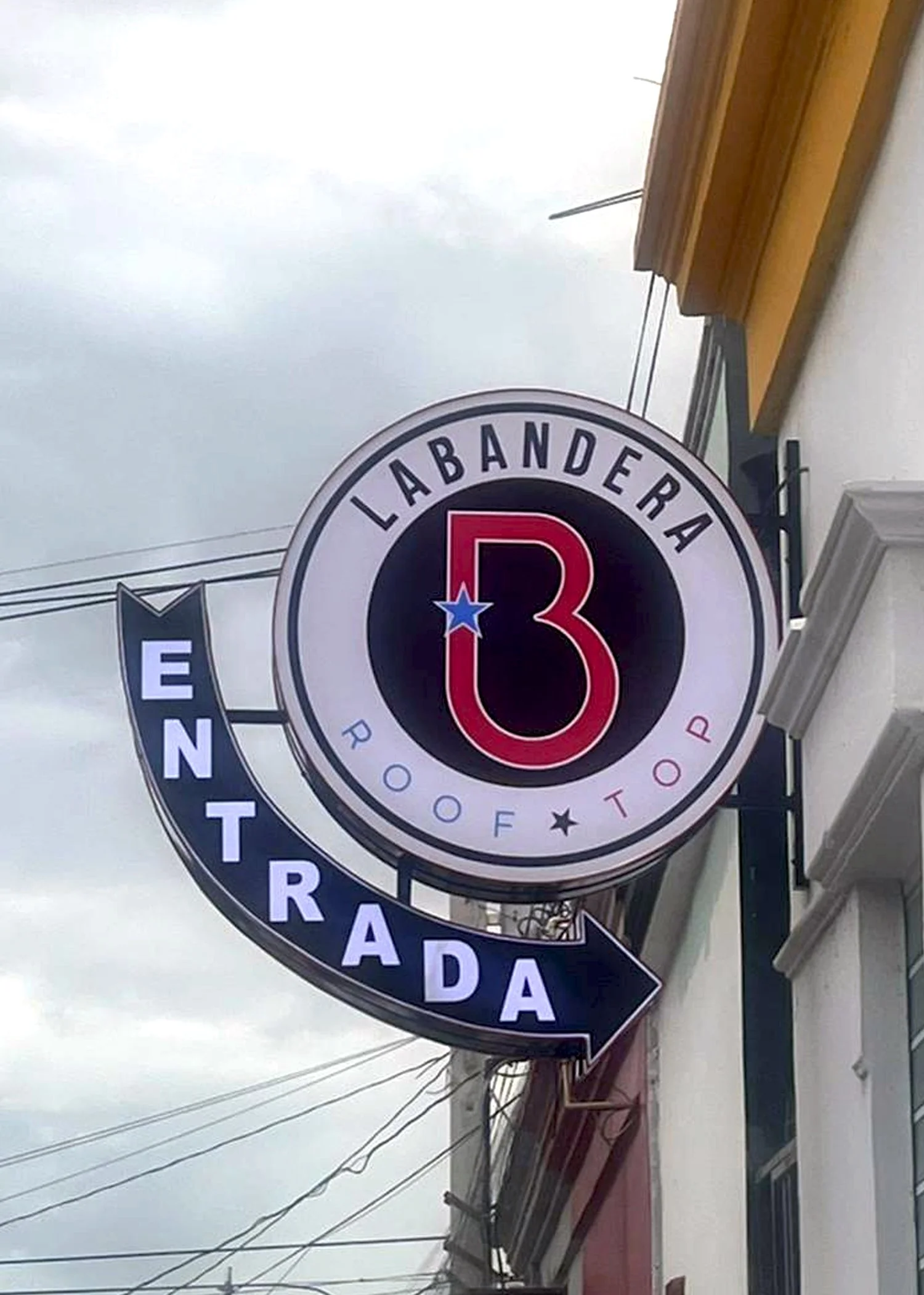 Señal de señalización con letras en español que dice 'LÁBARANDERA', en un entorno urbano con cables eléctricos en el cielo nublado