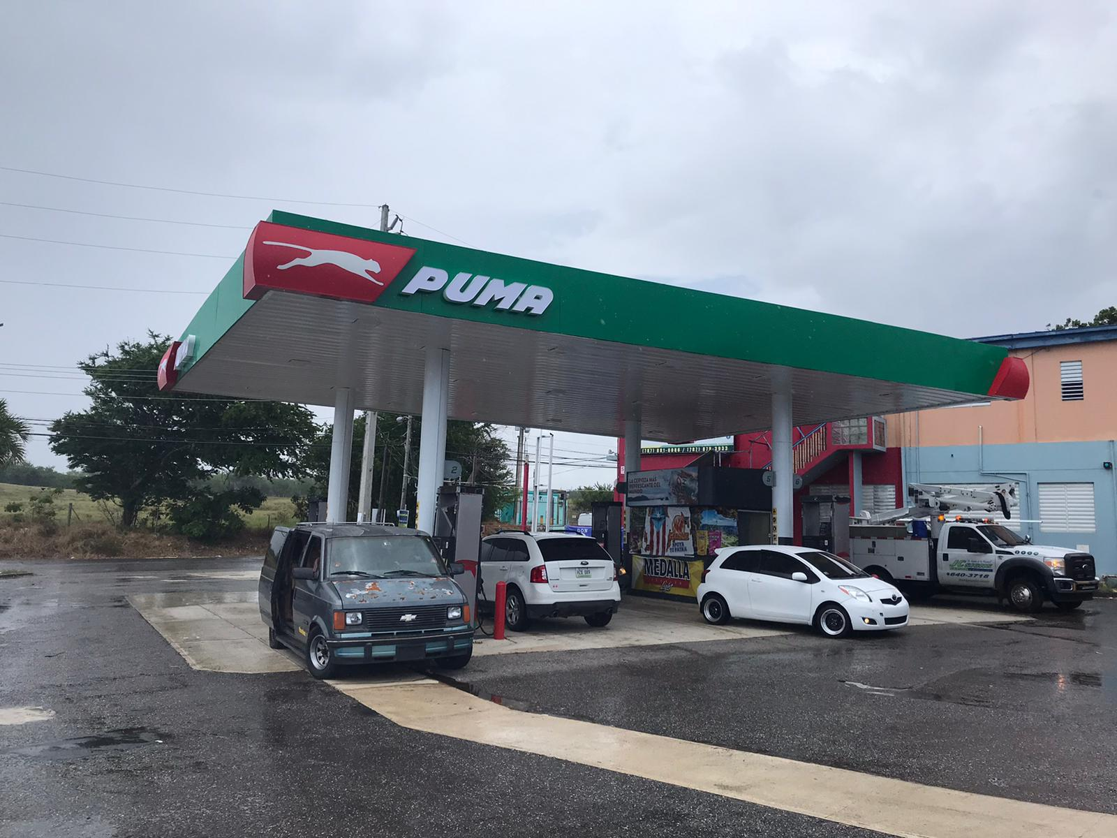 Estación de gasolina Puma con varios autos estacionados bajo el toldo, en un día nublado.