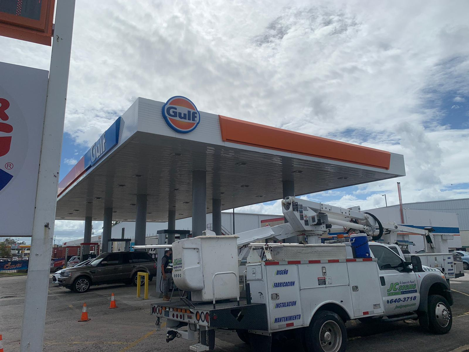 Estación de servicio con logotipo de Gulf, un camión de servicio en reparación y un coche estacionado.