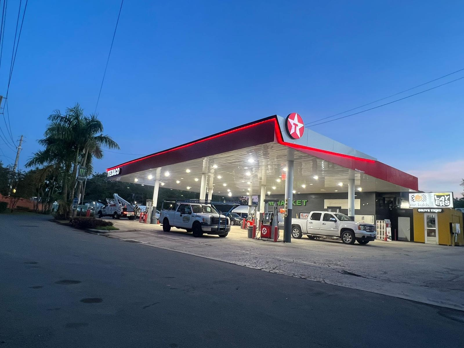 Estación de gasolina Texaco con varias autos en la bomba durante el atardecer, con palmeras y un cielo despejado.