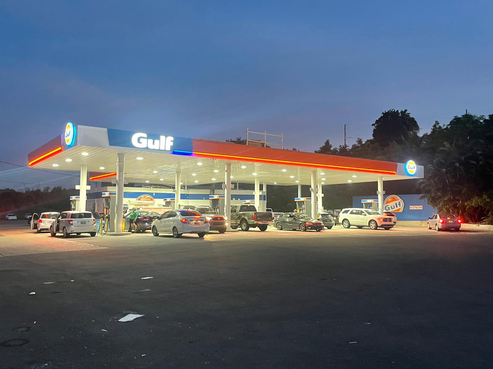 Estación de gasolina Gulf iluminada por la noche con varios vehículos estacionados y en proceso de cargar gasolina.