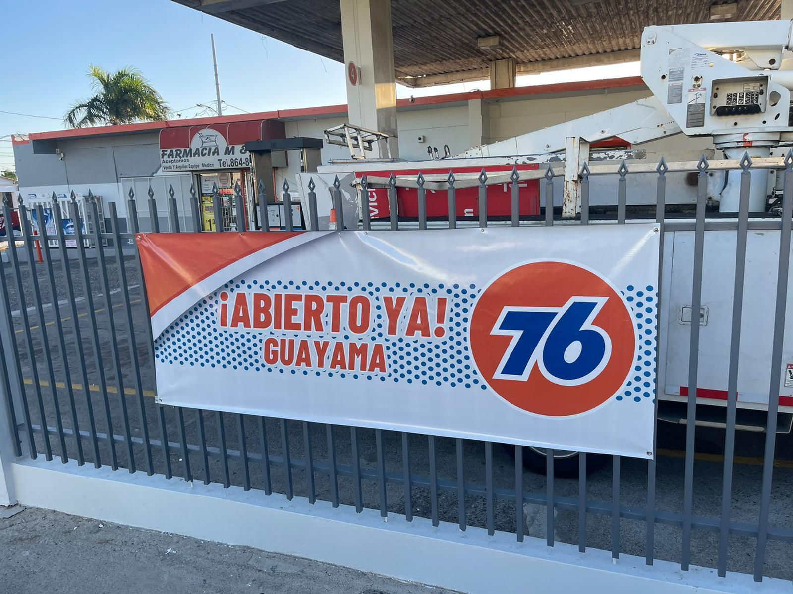 Cartel que anuncia la reapertura de una gasolinera con la frase en español ¡Abierto ya! Guayama, con el logo de la estación de gasolina 76. La gasolinera está detrás de una cerca de varillas de metal.