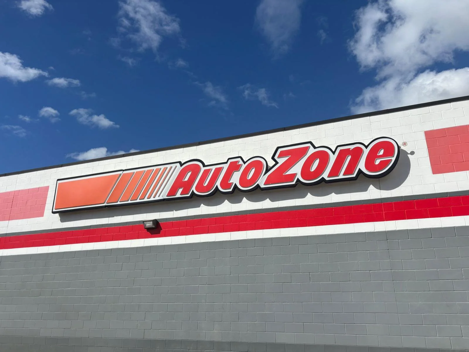 Vista del letrero de un centro comercial AutoZone en la fachada de un edificio con un cielo azul y algunas nubes.