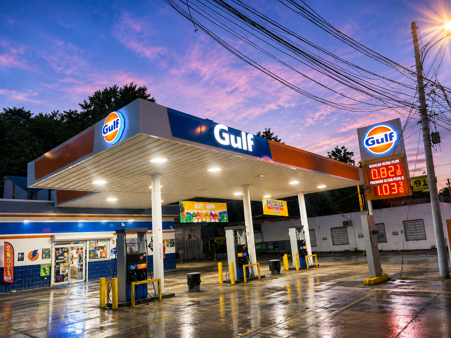 Estación de servicio Gulf con surtidores de gasolina bajo un cielo rosa y azul al atardecer, con cartel de precios de gasolina y cables eléctricos en la parte superior.