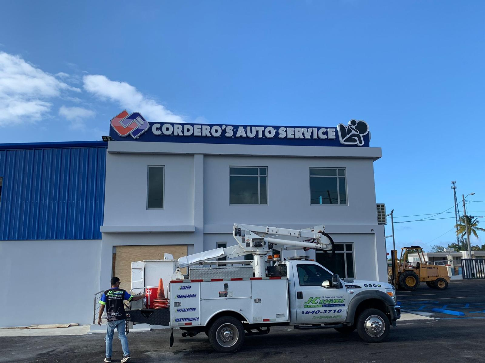 Edificio con señal de 'Cordero's Auto Service' y trabajadores en una camioneta de servicio técnico. 