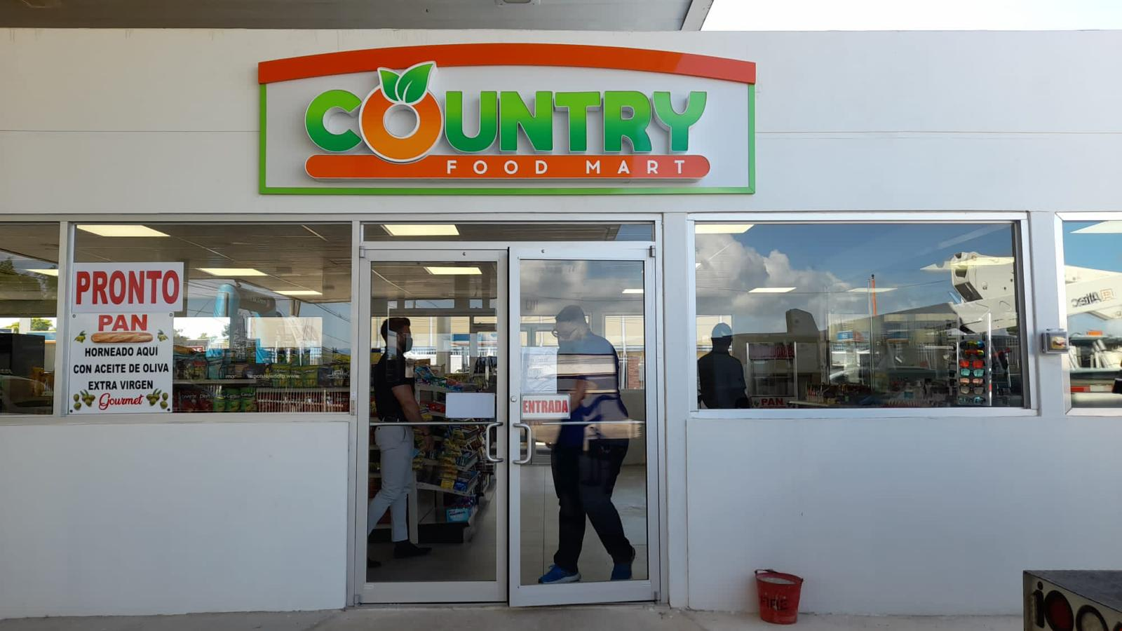 Entrada de supermercado llamado 'Country Food Mart', con un cartel que dice 'Pronto Pan, Horneado aquí con aceite de oliva extra virgen'.