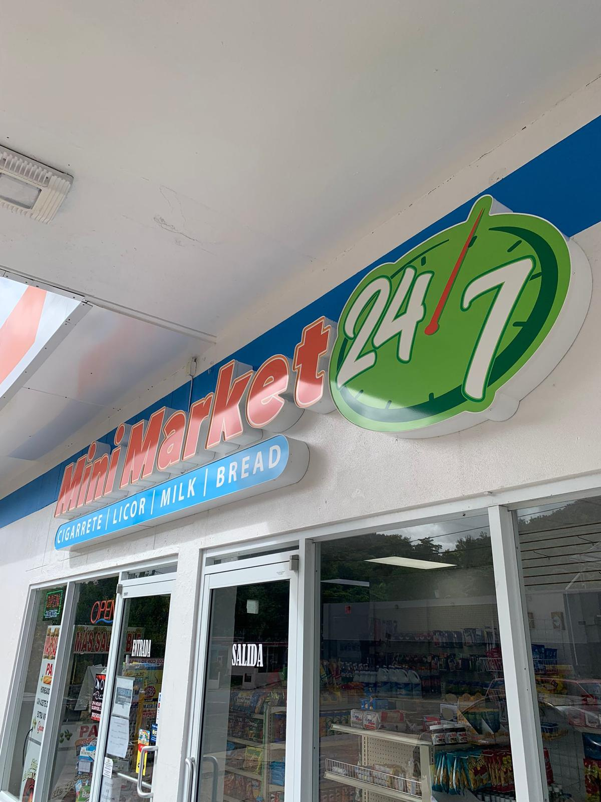 Cartel de tienda de conveniencia que dice 'Mini Market 24/7' y 'Cigarrete, Licor, Milk, Bread' con reloj que indica las 12 en punto.
