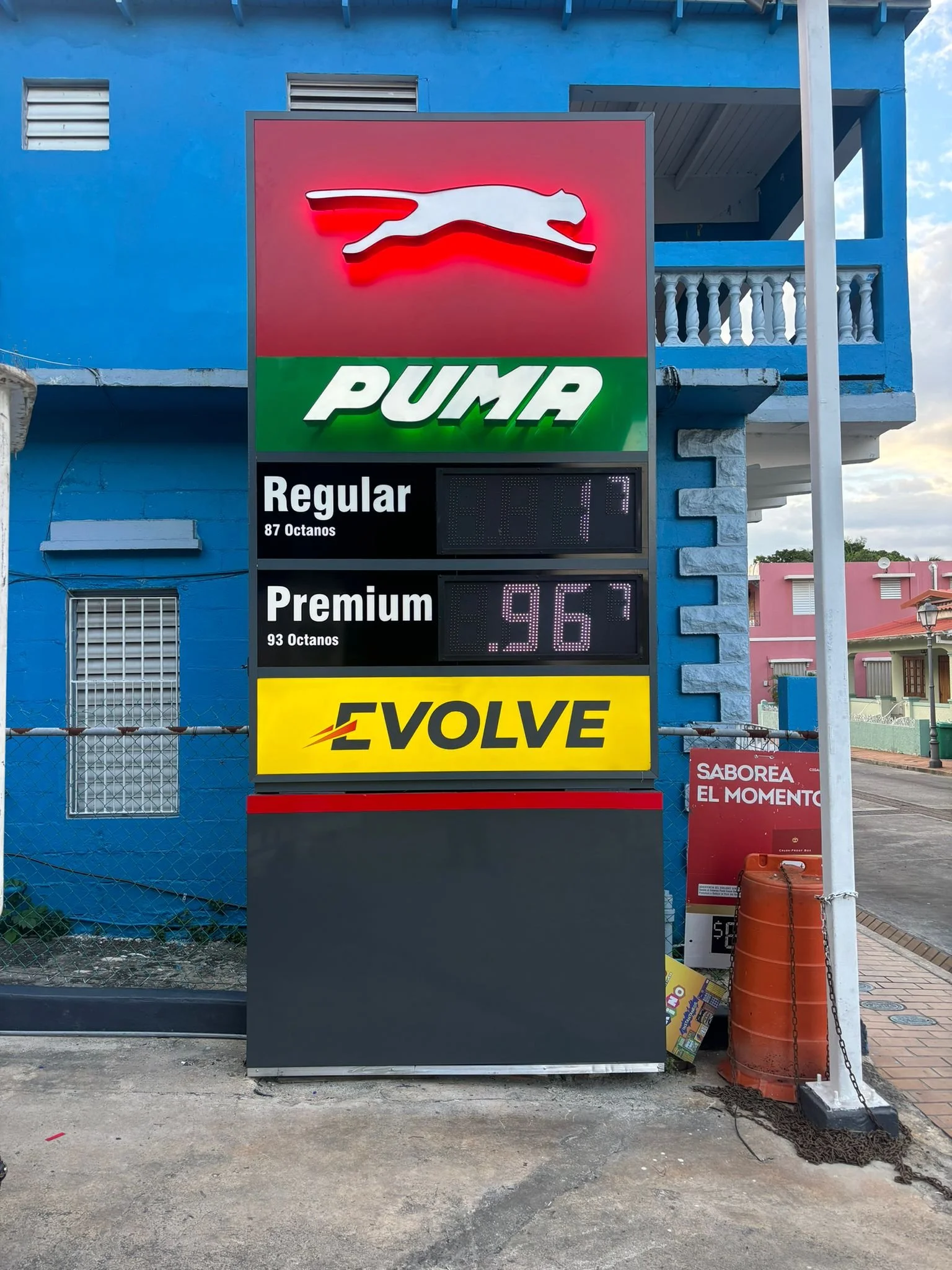 Estación de gasolina con cartel de la marca Puma, mostrando precios de gasolina regular y premium y un letrero amarillo con la palabra 'Evolve'.