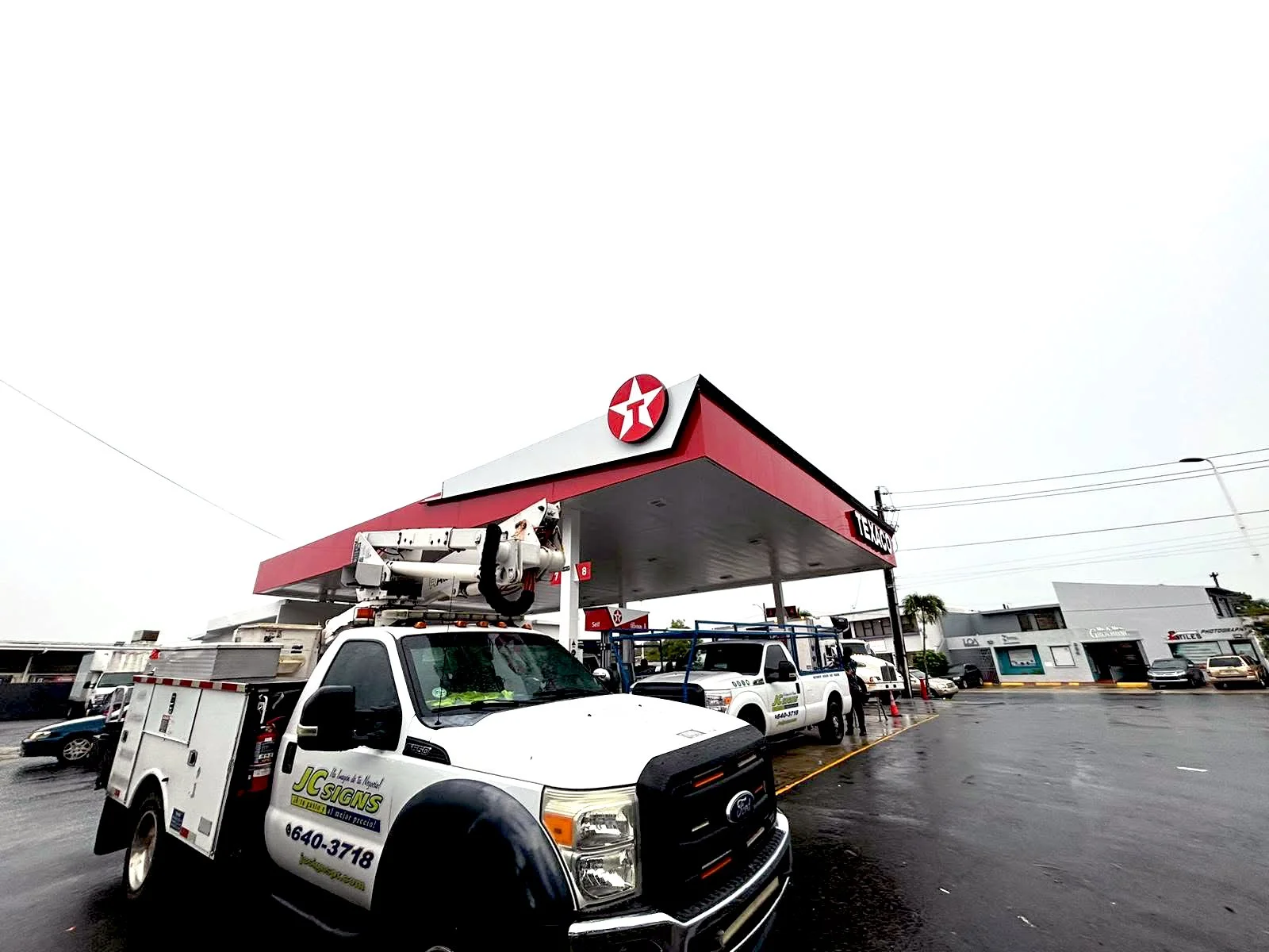 Una estación de gasolina con un vehículo de servicios técnicos y varias personas. 