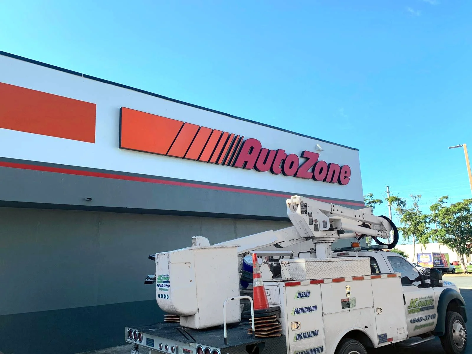 Una fletera con equipo de trabajo en un estacionamiento en un día soleado y cielo despejado frente a un edificio de AutoZone.