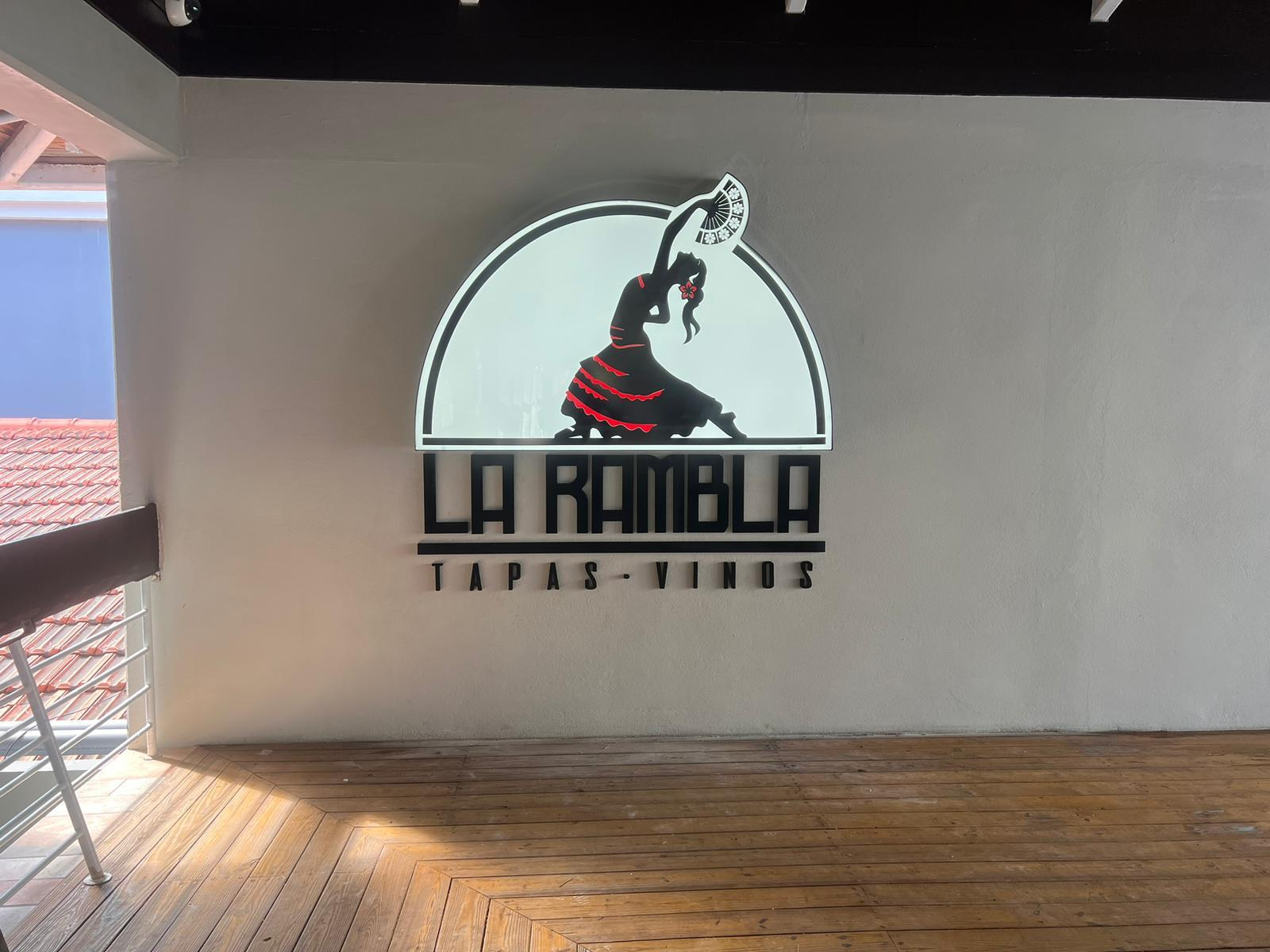 Cartel iluminado de un restaurante llamado La Rambla, con un diseño de bailarina andaluza y la leyenda 'Tapas - Vinos'.