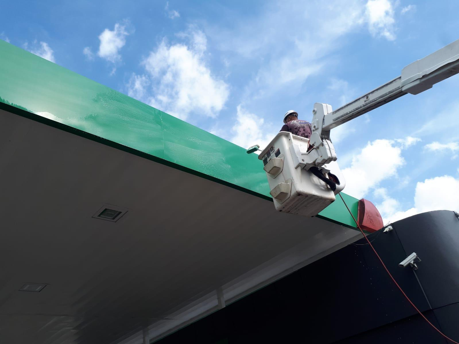 Trabajador en elevador realizando mantenimiento en la parte superior de un edificio con cielo azul y nubes.