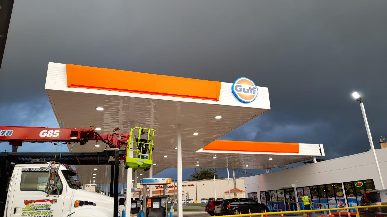 Estación de gasolina Gulf en construcción o mantenimiento, con un andambré y una linterna en el lugar, y un cielo nublado al fondo.