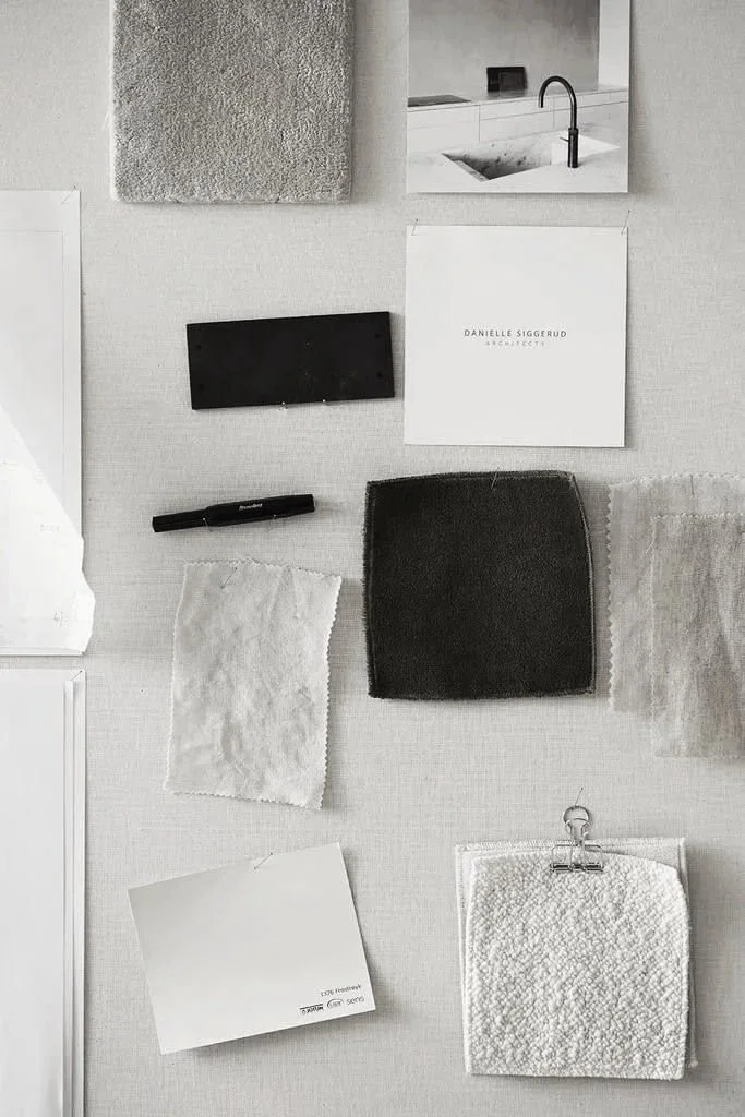 Flat lay of interior design materials including fabric swatches, paint samples, a pen, a notebook, and a towel, on a light-colored surface.