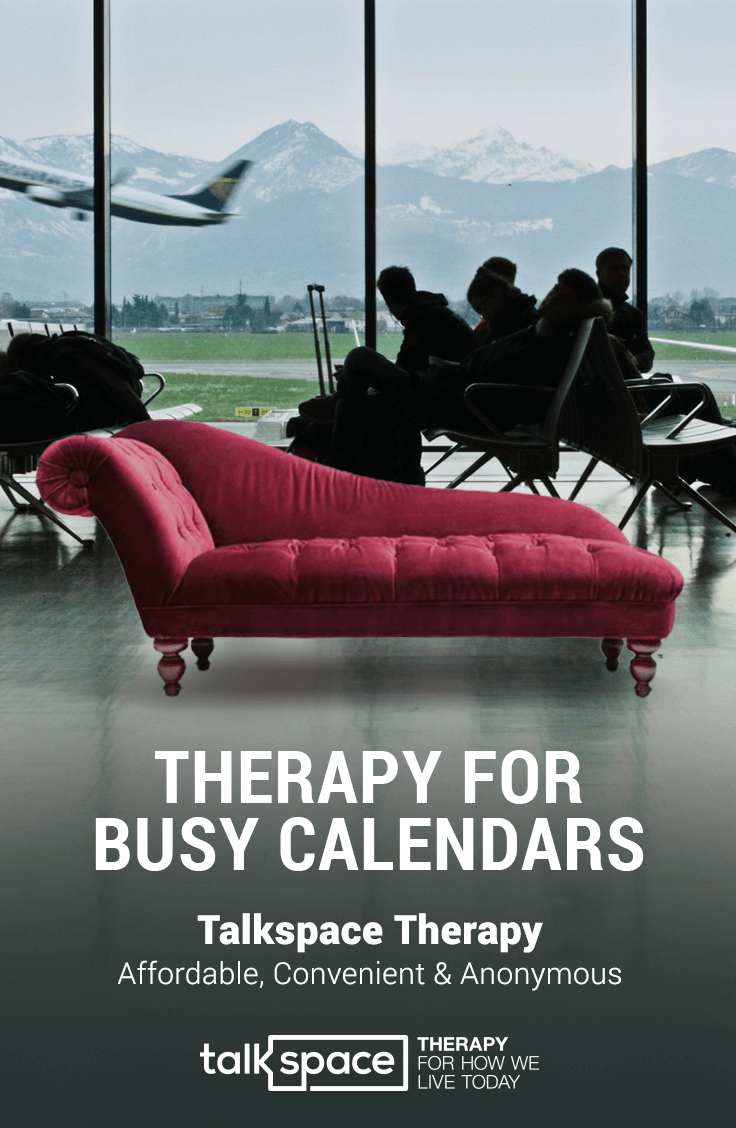 A red vintage chaise lounge chair inside an airport terminal with glass windows showing an airplane taking off and snow-capped mountains in the background.