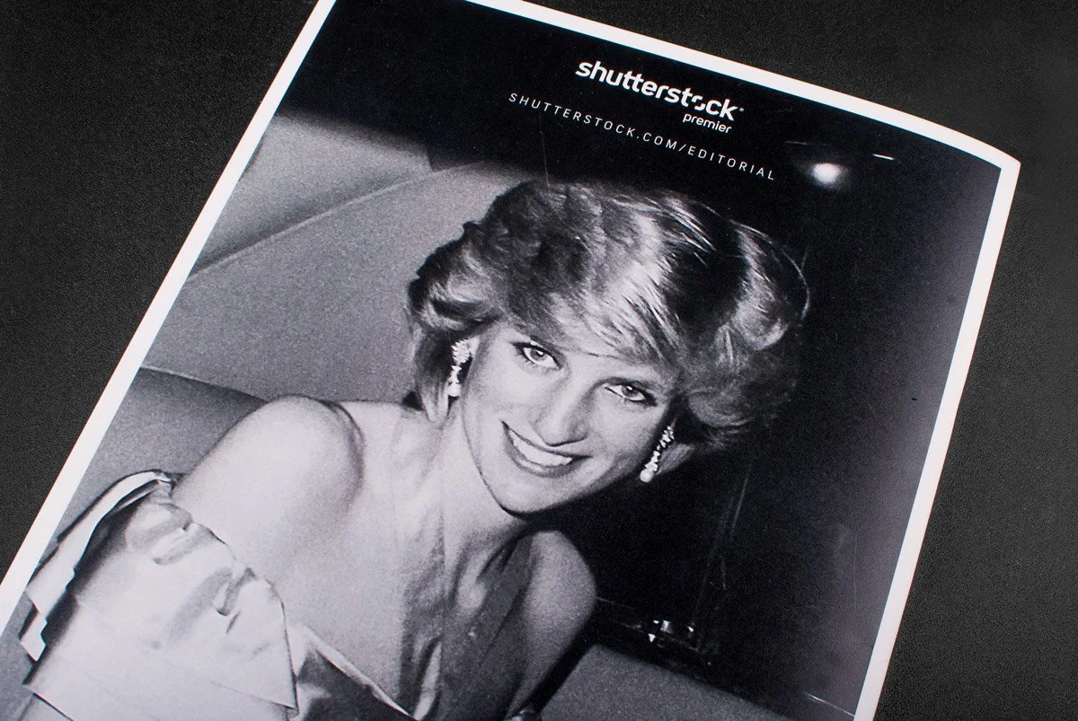 Black and white photo of a smiling woman with voluminous hair, wearing earrings and an off-the-shoulder dress, on a printed page with the Shutterstock logo at the top.