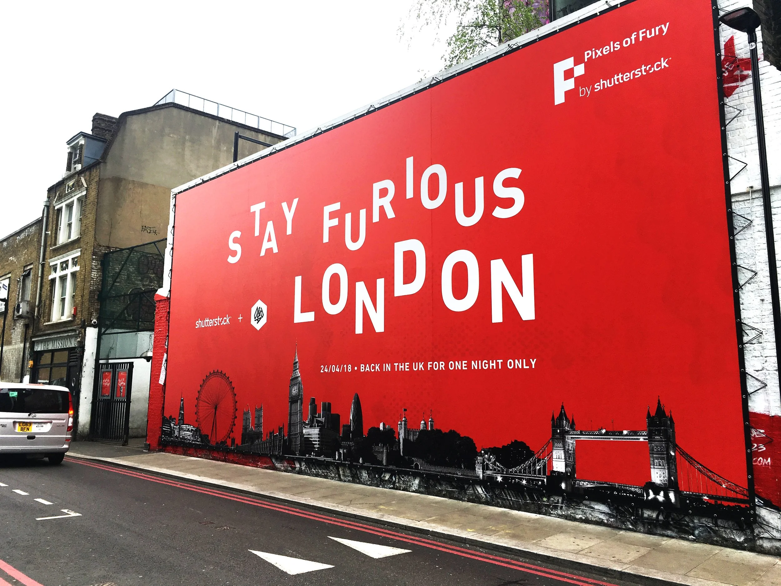 A large red billboard promoting a one-night return visit to London on April 24, 2018, featuring silhouettes of London landmarks like Big Ben and the London Eye, with the background cityscape and a street in the foreground.