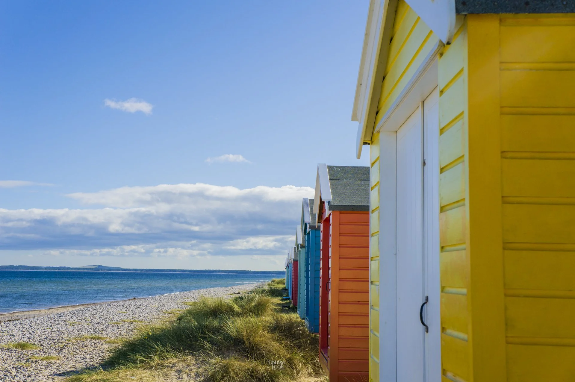 A row of colourful beach huts are the focus of this beautiful calm and serene landscape photo of Findhorn on the Moray Coast of Scotland. This image is a popular choice for wall art for holiday lets in Moray Speyside.