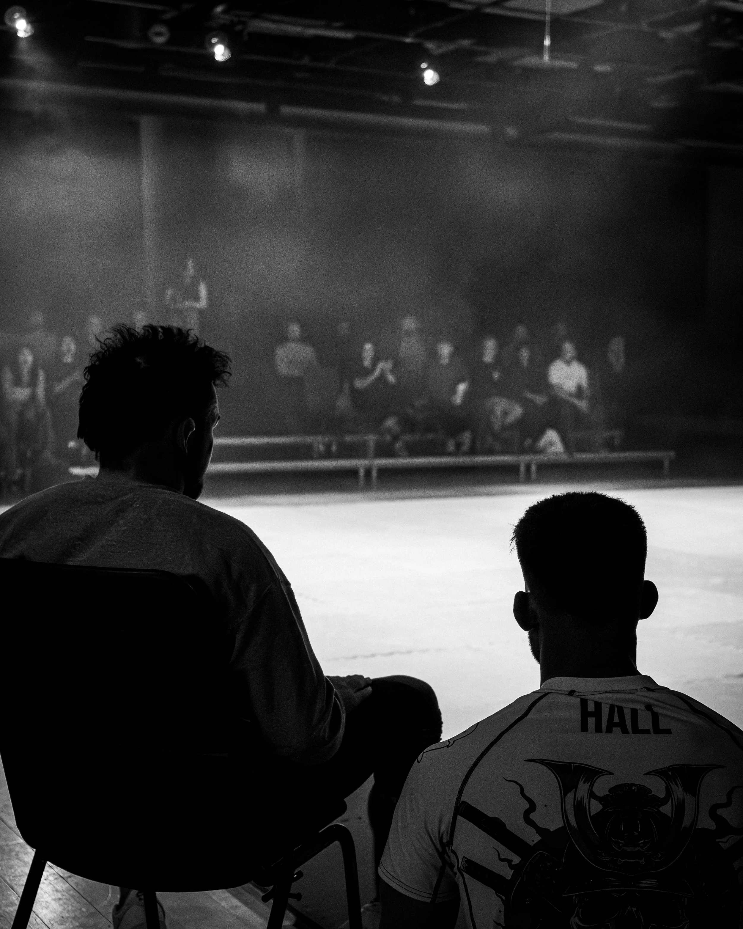 People sitting in a dark room watching a large screen with black and white video projection.