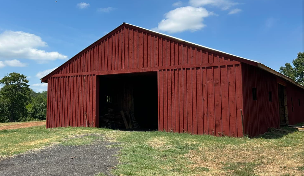 A red barn with a sloped roof on a grassy field under a partly cloudy sky.