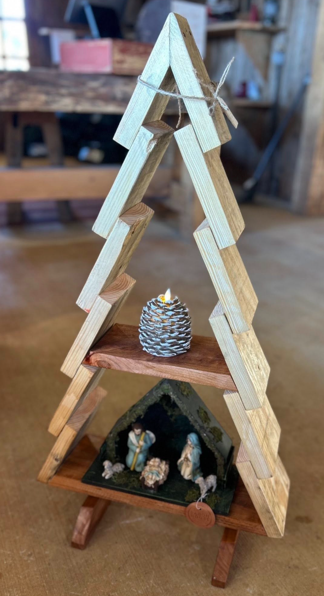 Small wooden Christmas pyramid with figurines of Mary, Joseph, and baby Jesus in a nativity scene, a pinecone candle in the middle, and wooden ladder-like tiers on a rustic table.