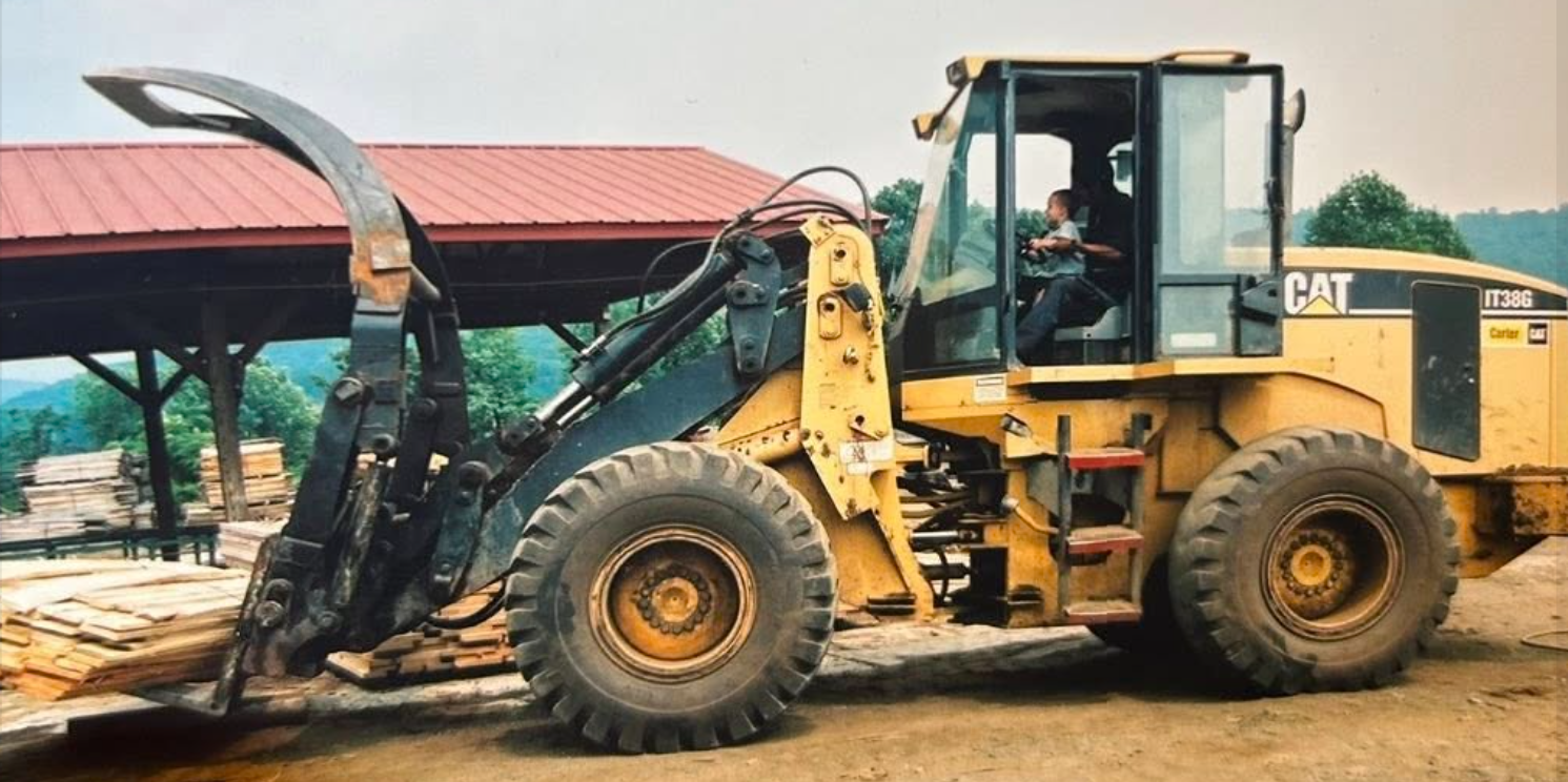 A yellow CAT forklift carrying a load of wooden planks at a lumber yard.