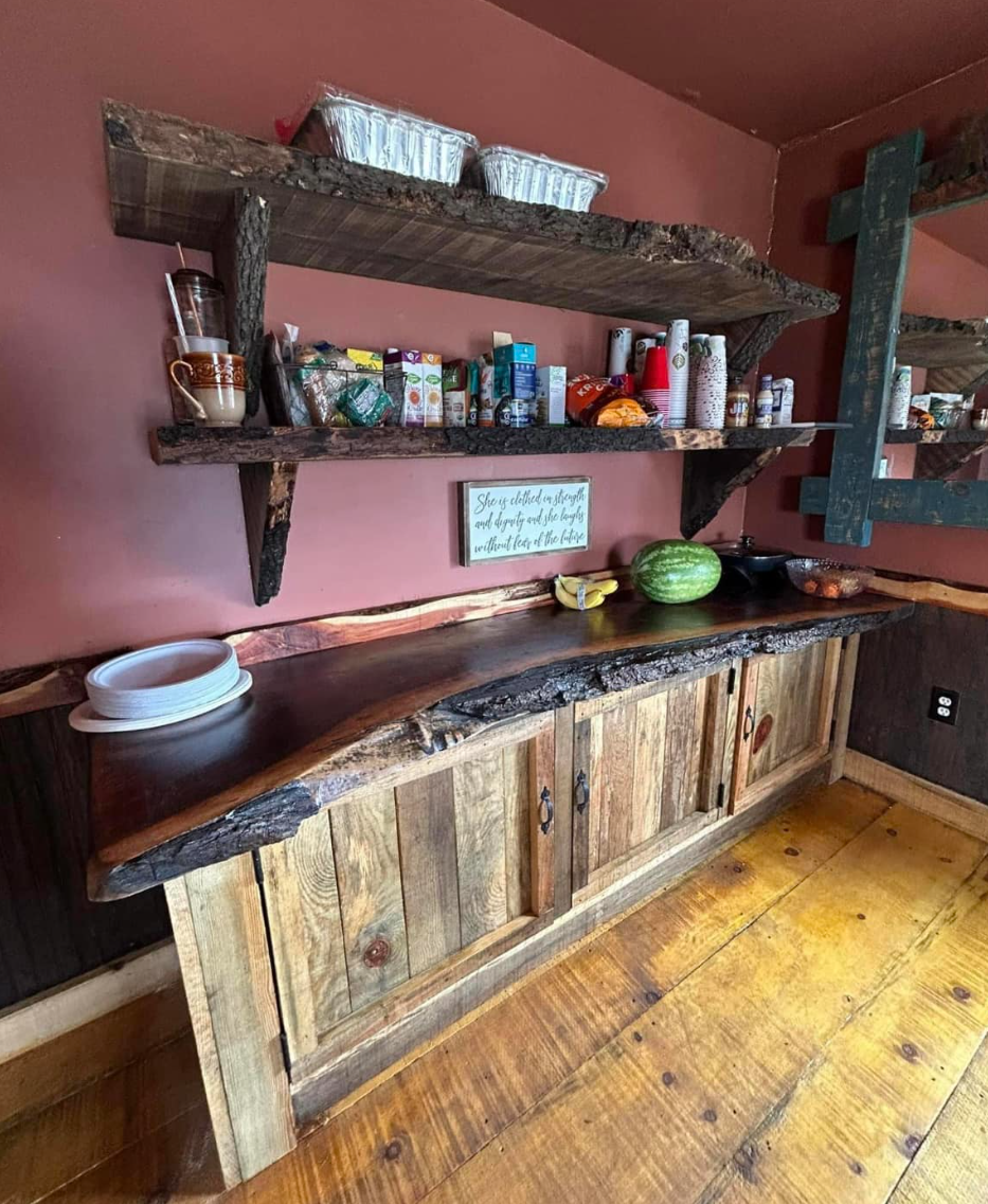 Rustic kitchen shelf with snacks, cups, and containers above a wooden countertop and cabinets on a pink wall.