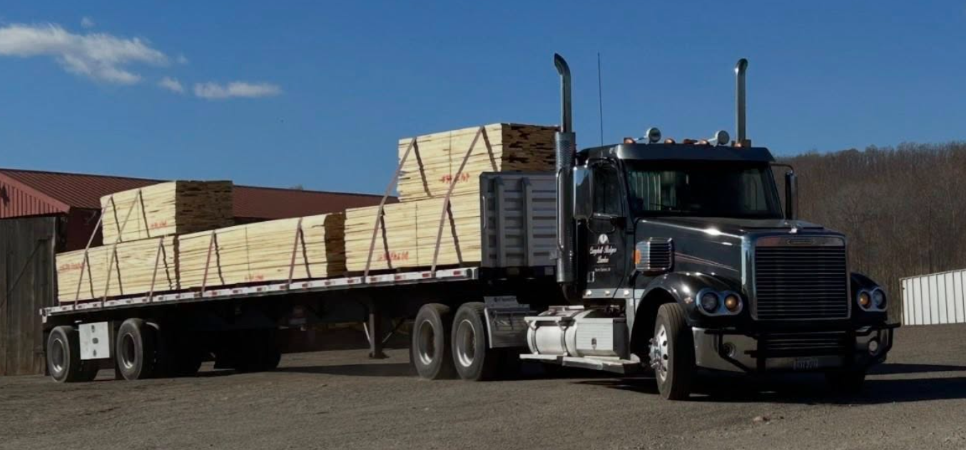 Black semi-truck carrying oversized stacks of lumber on a flatbed trailer