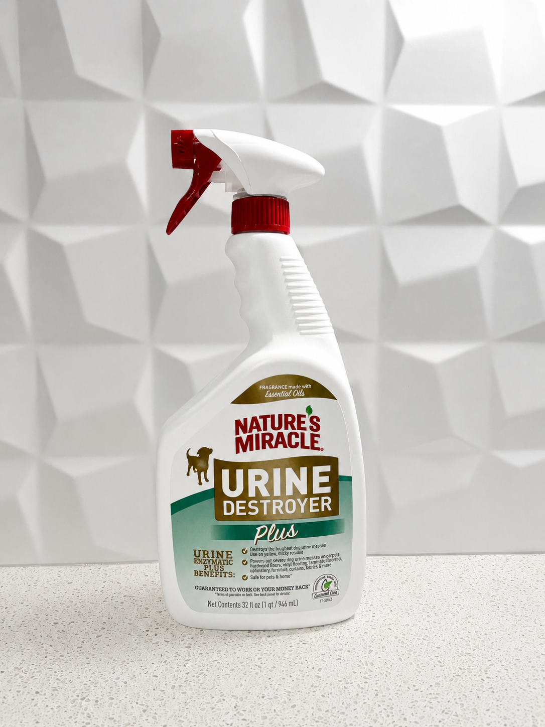 A white spray bottle labeled 'Nature's Miracle Urine Destroyer Plus' with a red trigger spray nozzle, standing on a speckled countertop against a textured white wall.