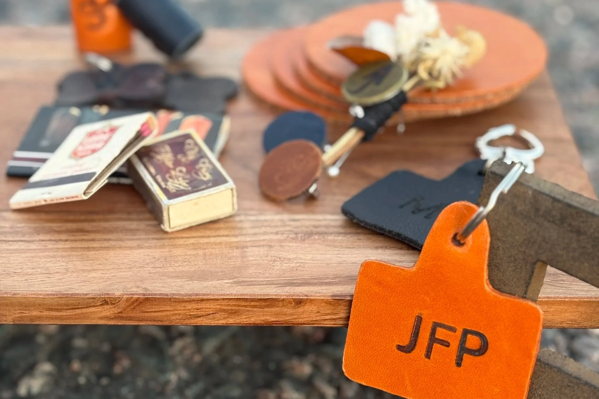 Close-up of a wooden outdoor table with matchbook decorations, a monogrammed boutonniere pin, and Keychain shaped like cattle tag with monogram "JFP".