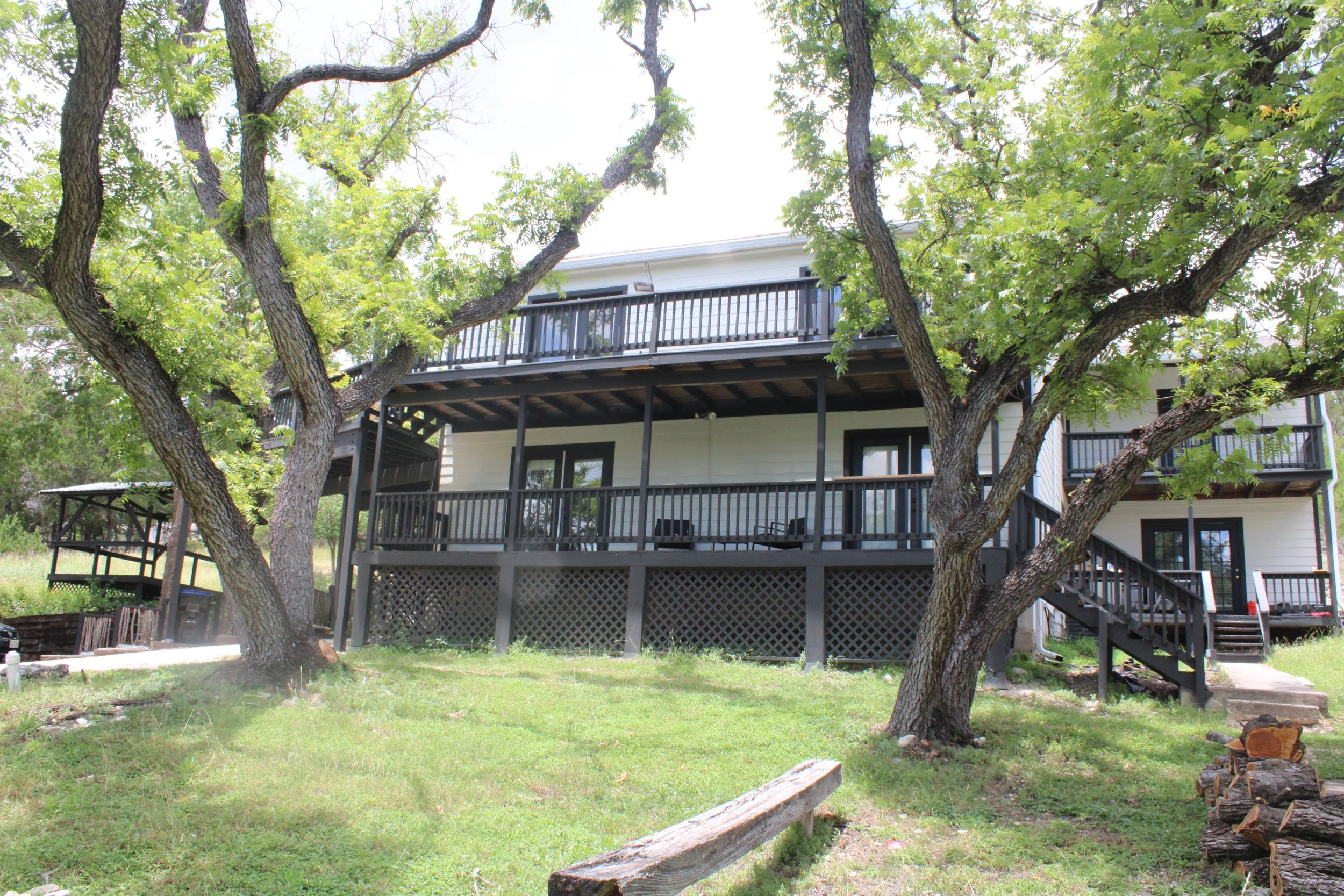 A two-story house with a large balconies, surrounded by green trees and a grassy yard.