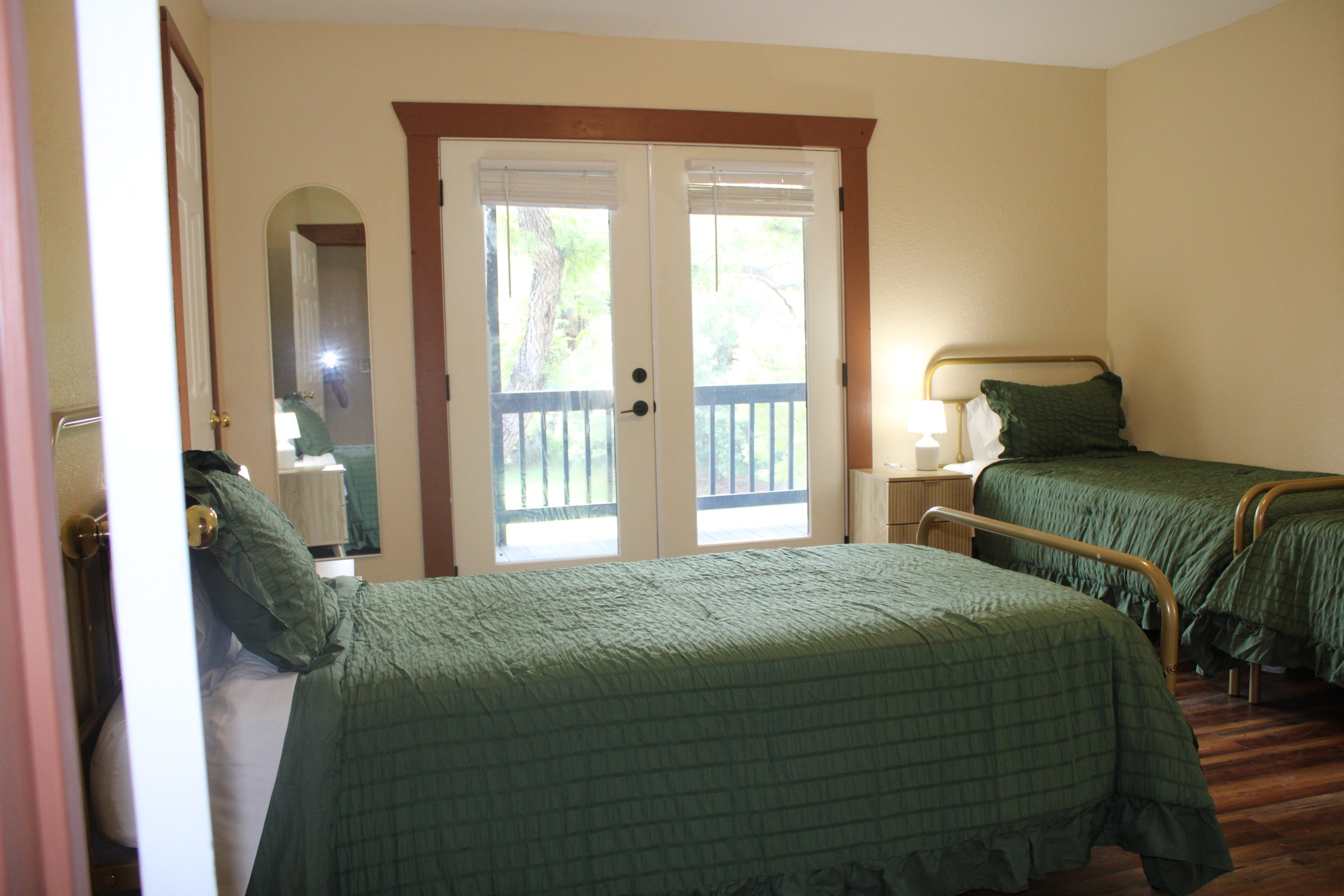 A bedroom with twin beds covered in green quilts, pillows, and white sheets. Each bed has a small nightstand with a white lamp. We provide bedding