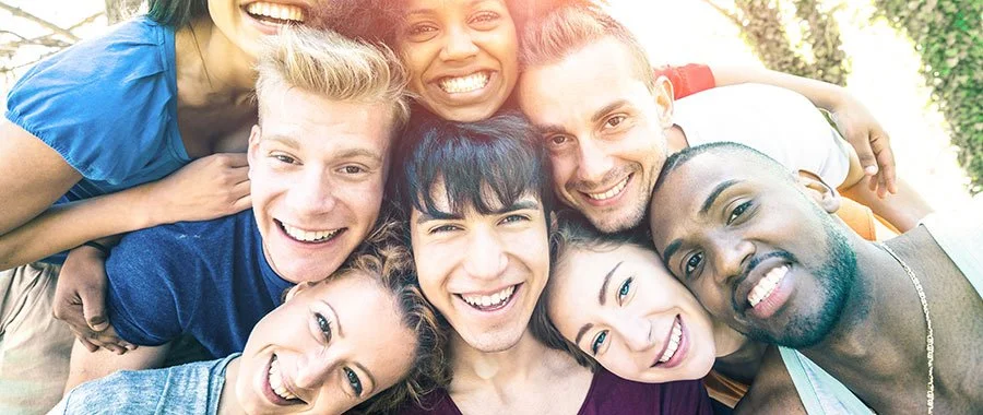 A group of eight diverse young adults smiling together in an outdoor setting.