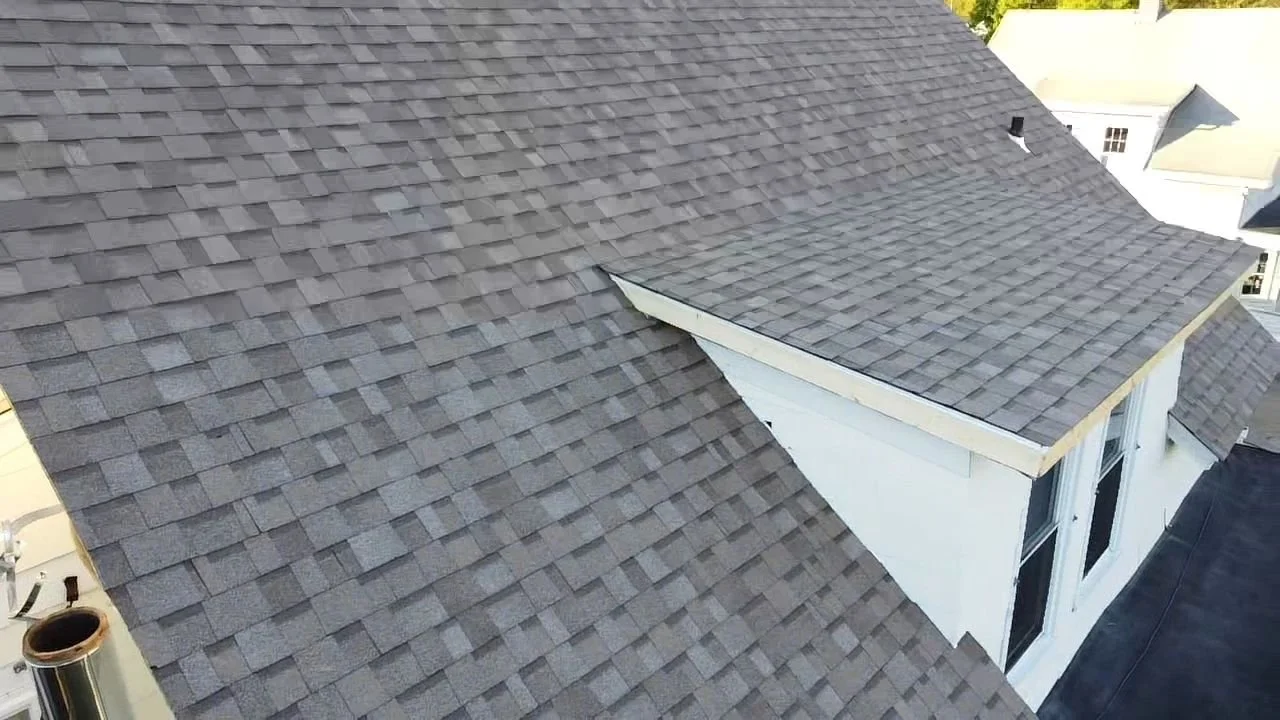 Aerial view of a house roof with gray asphalt shingles and white trim.