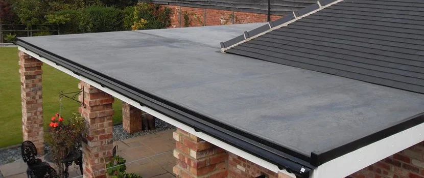 Close-up of a flat roof with a rubber membrane, adjacent to a sloped shingled roof on a brick house.