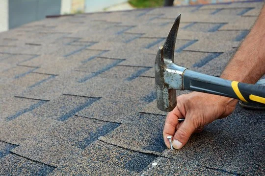 Close-up of a person using a hammer to fix or remove a shingle on a roof
