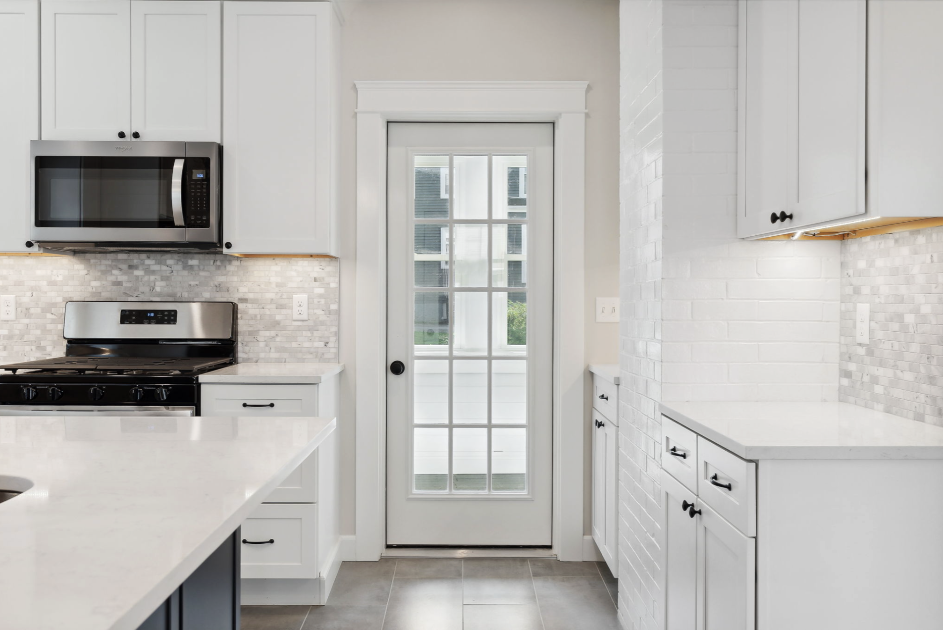 Kitchen with white cabinets, a stainless steel microwave, and a door with glass panels leading outside.