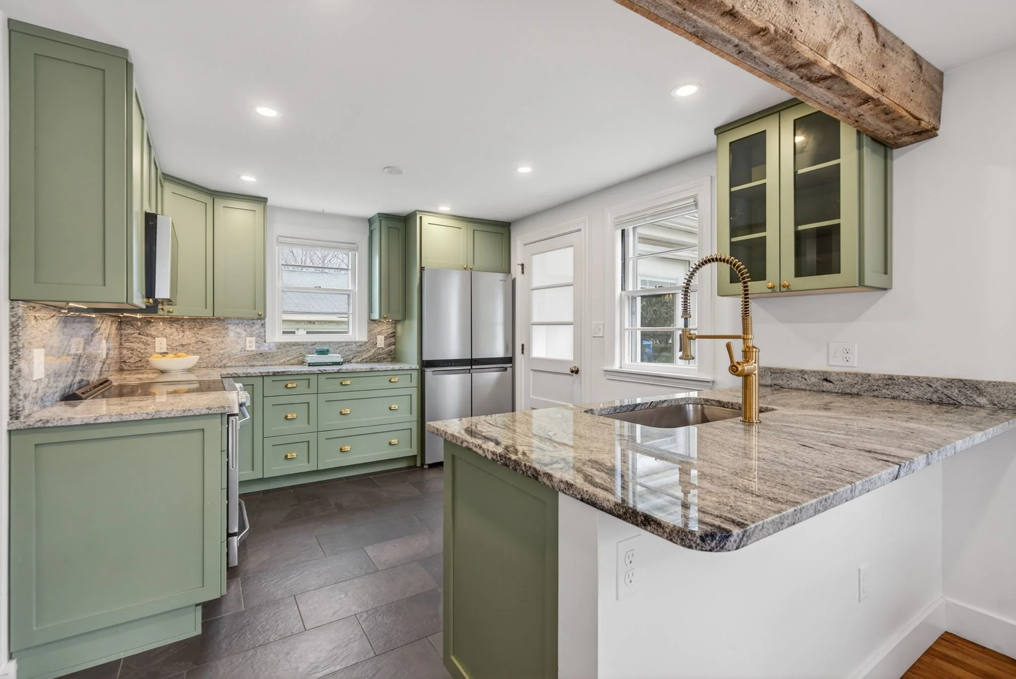 Modern kitchen with green cabinets, granite countertops, stainless steel appliances, and a gold faucet.