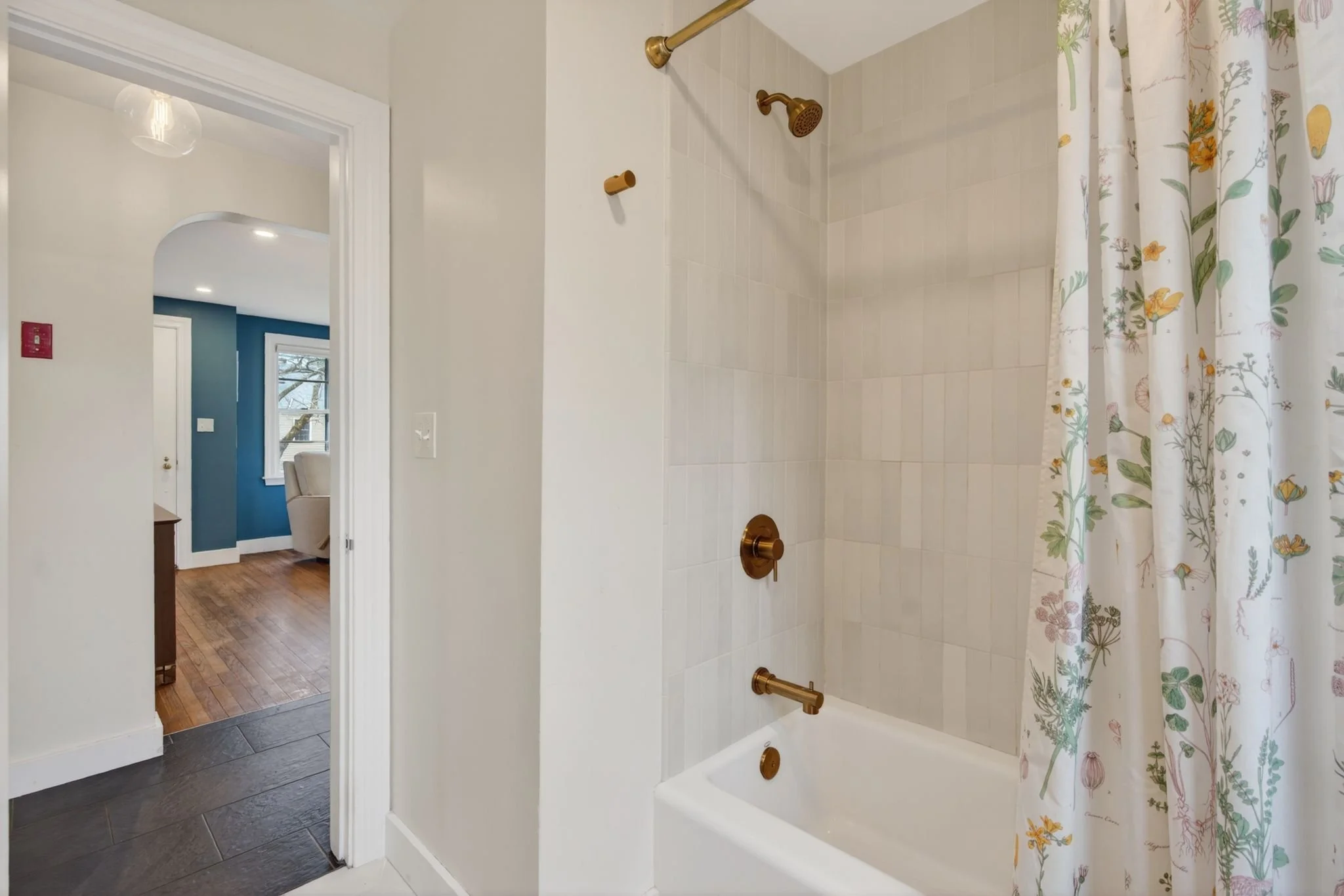 Inside view of a bathroom shower with beige tiles, brass fixtures, and a floral shower curtain.