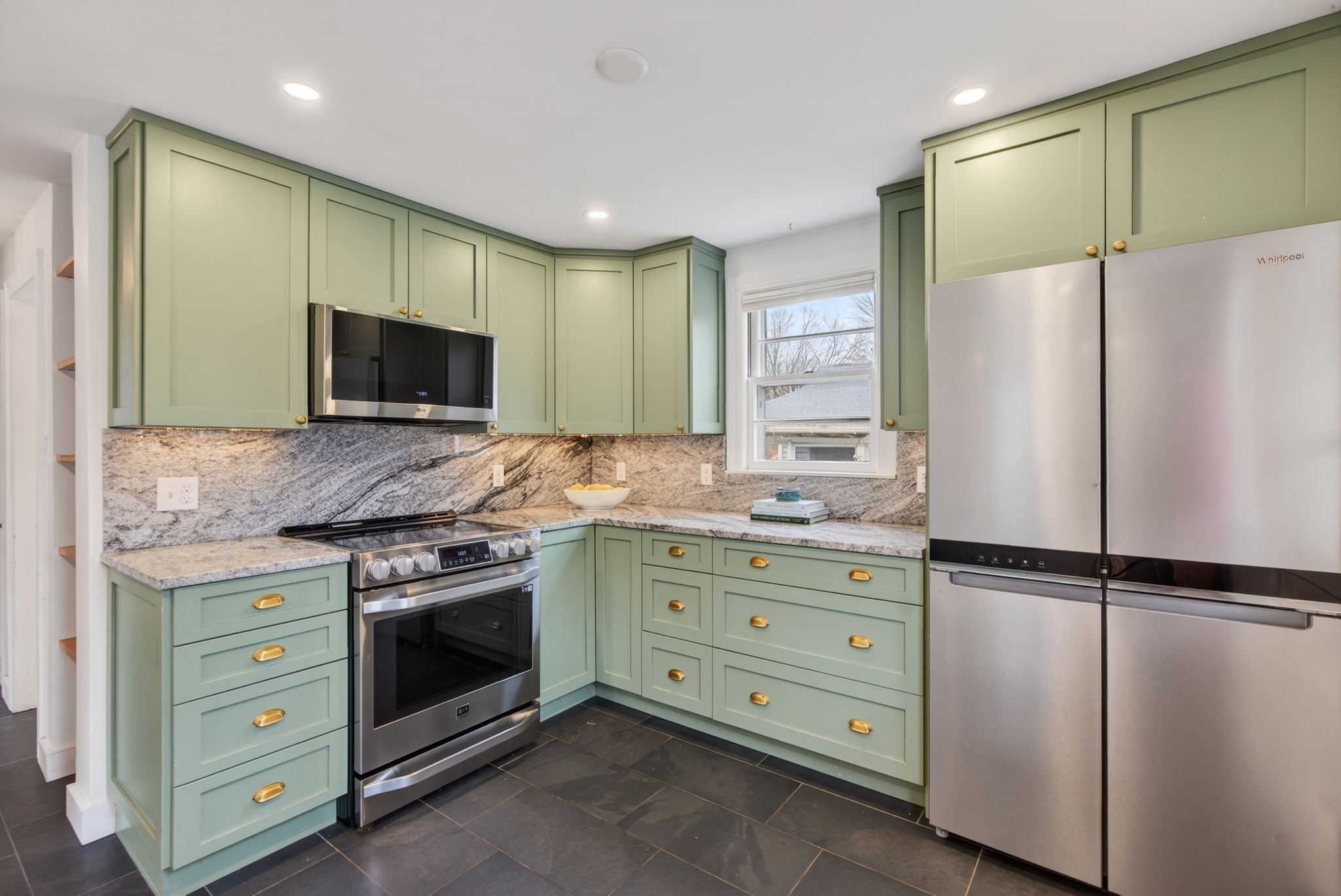 Kitchen with green cabinets, a stainless steel oven, a microwave, granite countertops, a window, and a stainless steel refrigerator.