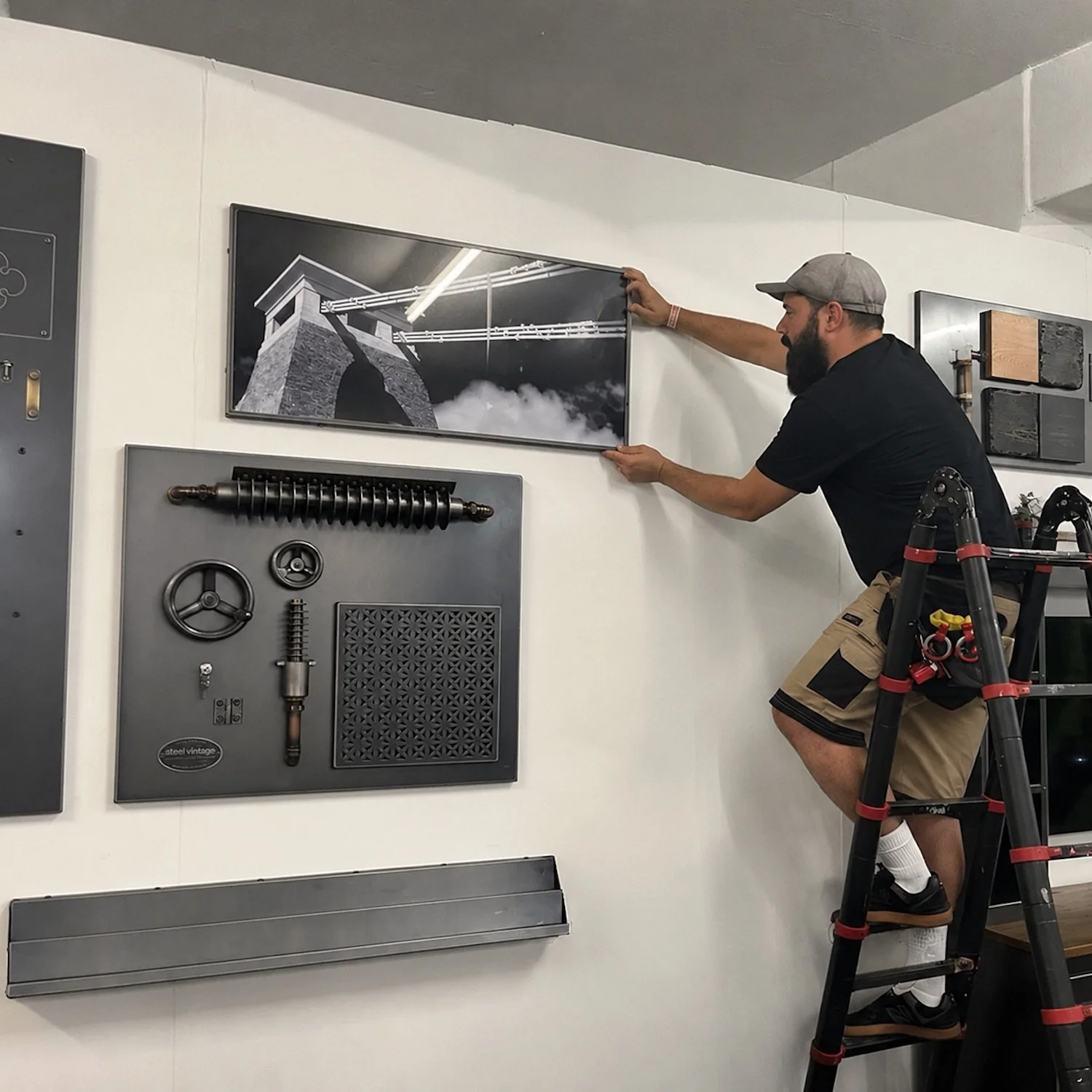 Alex from Ursa Major Install carefully hanging a framed picture on a showroom wall using professional installation techniques.