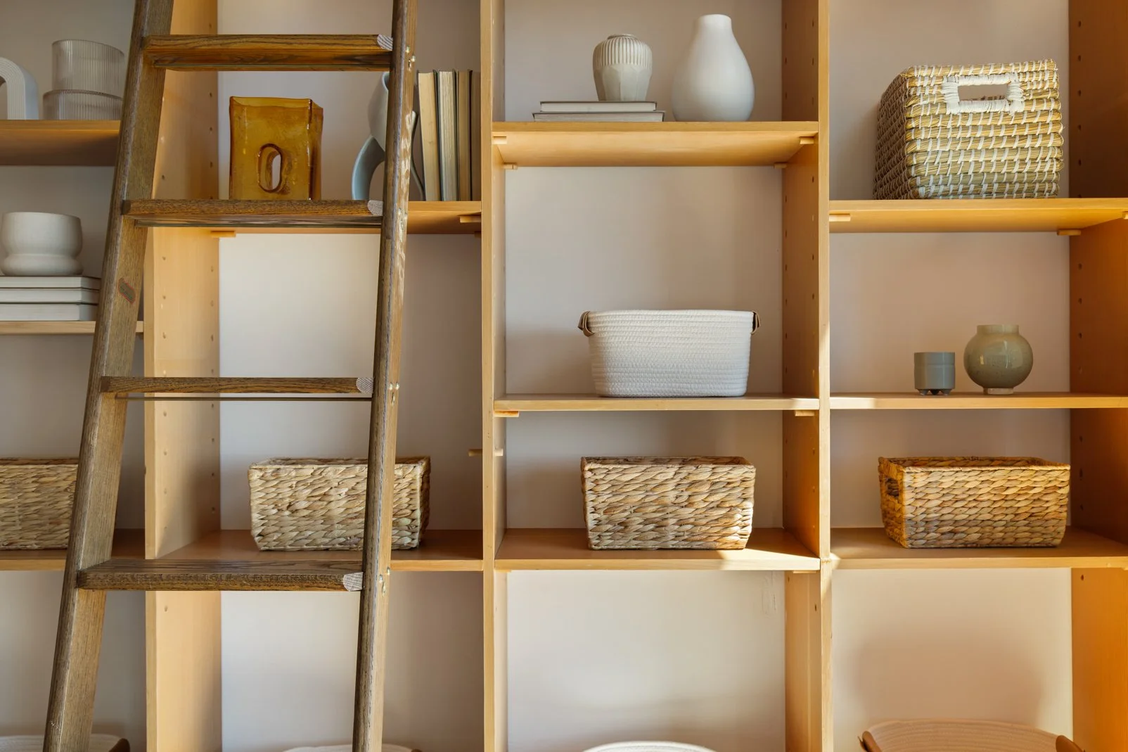Wooden shelving unit filled with woven baskets and minimalist decorative items. A wooden ladder leaning against the unit.