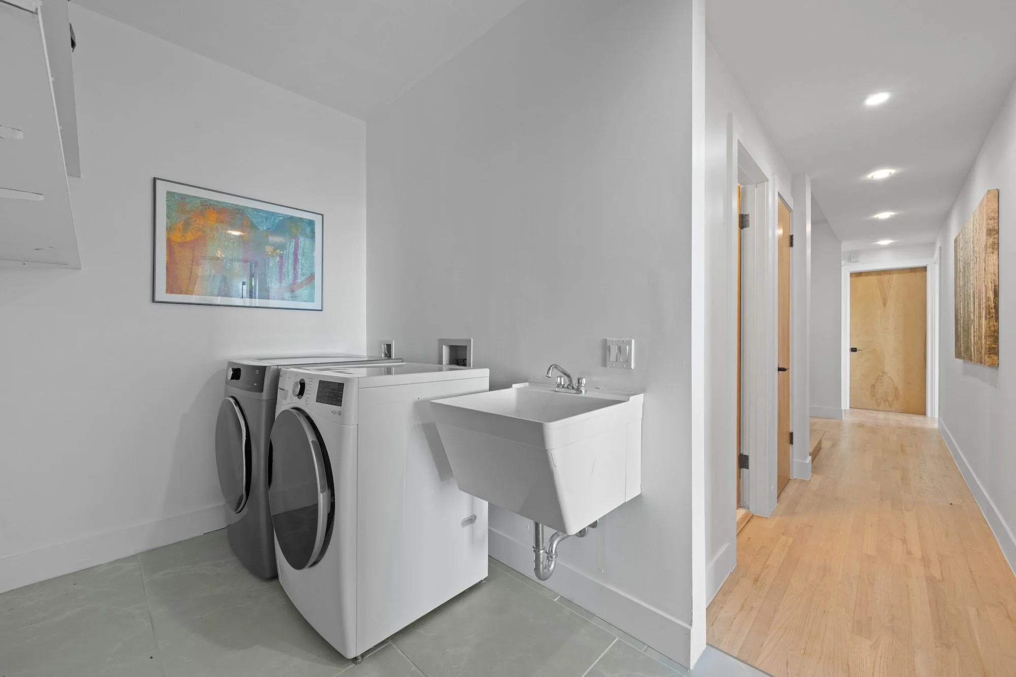 Laundry room with front-loading washer and dryer, utility sink, and framed artwork on white walls.