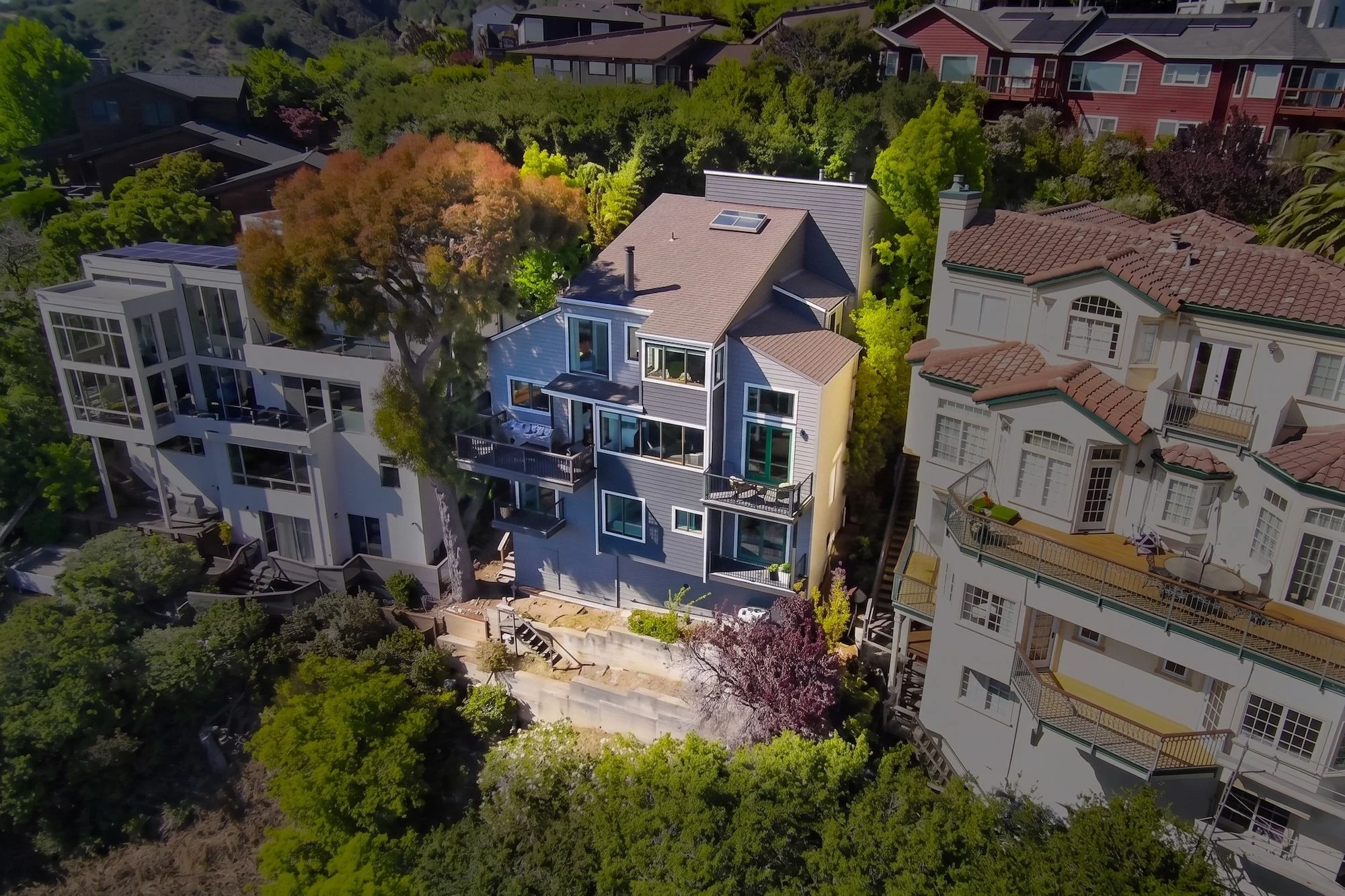Aerial view of a residential neighborhood with multi-story houses surrounded by lush green trees.