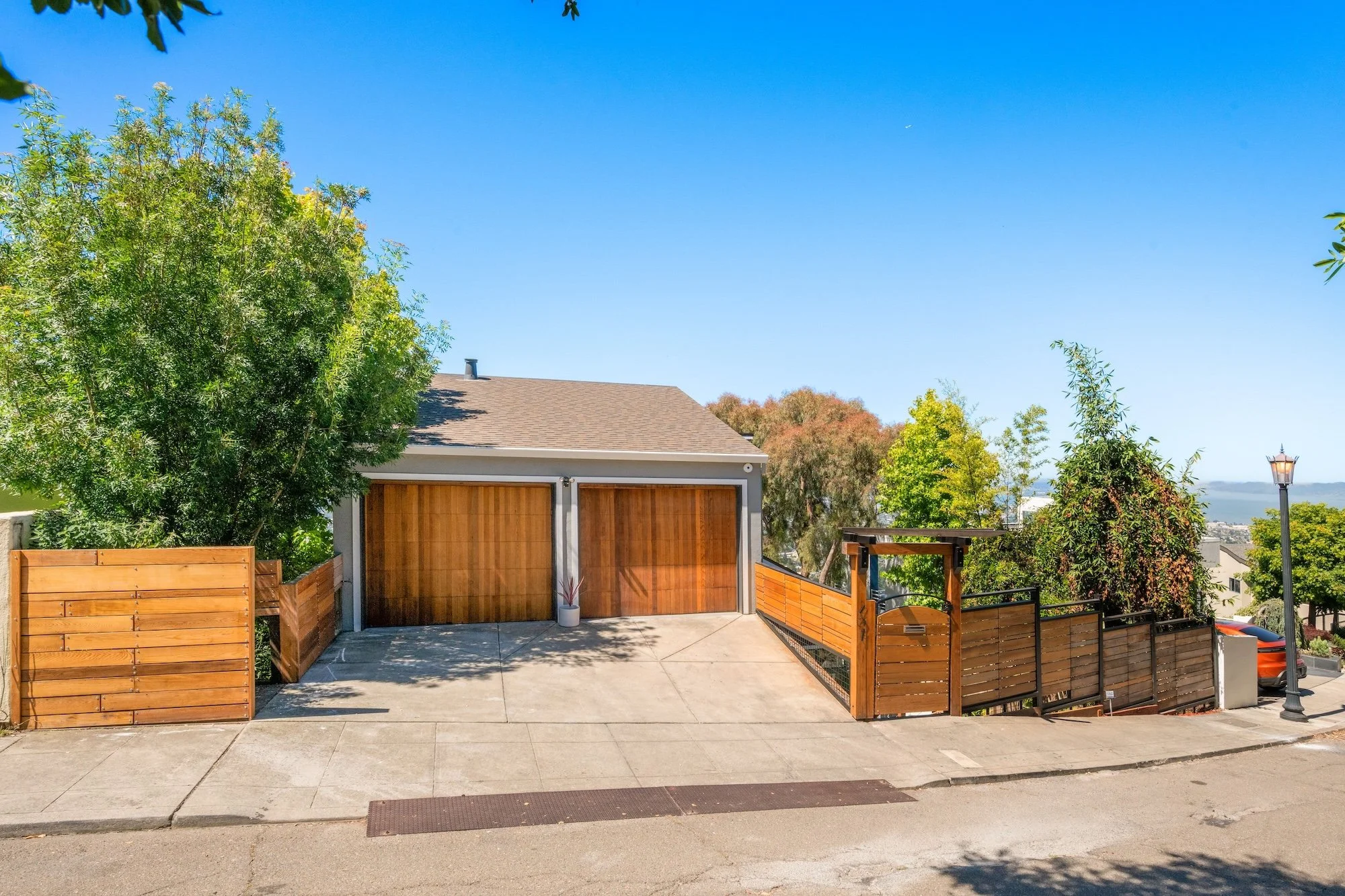Residential backyard with a wooden fence, concrete patio, garage, trees, and a clear blue sky.